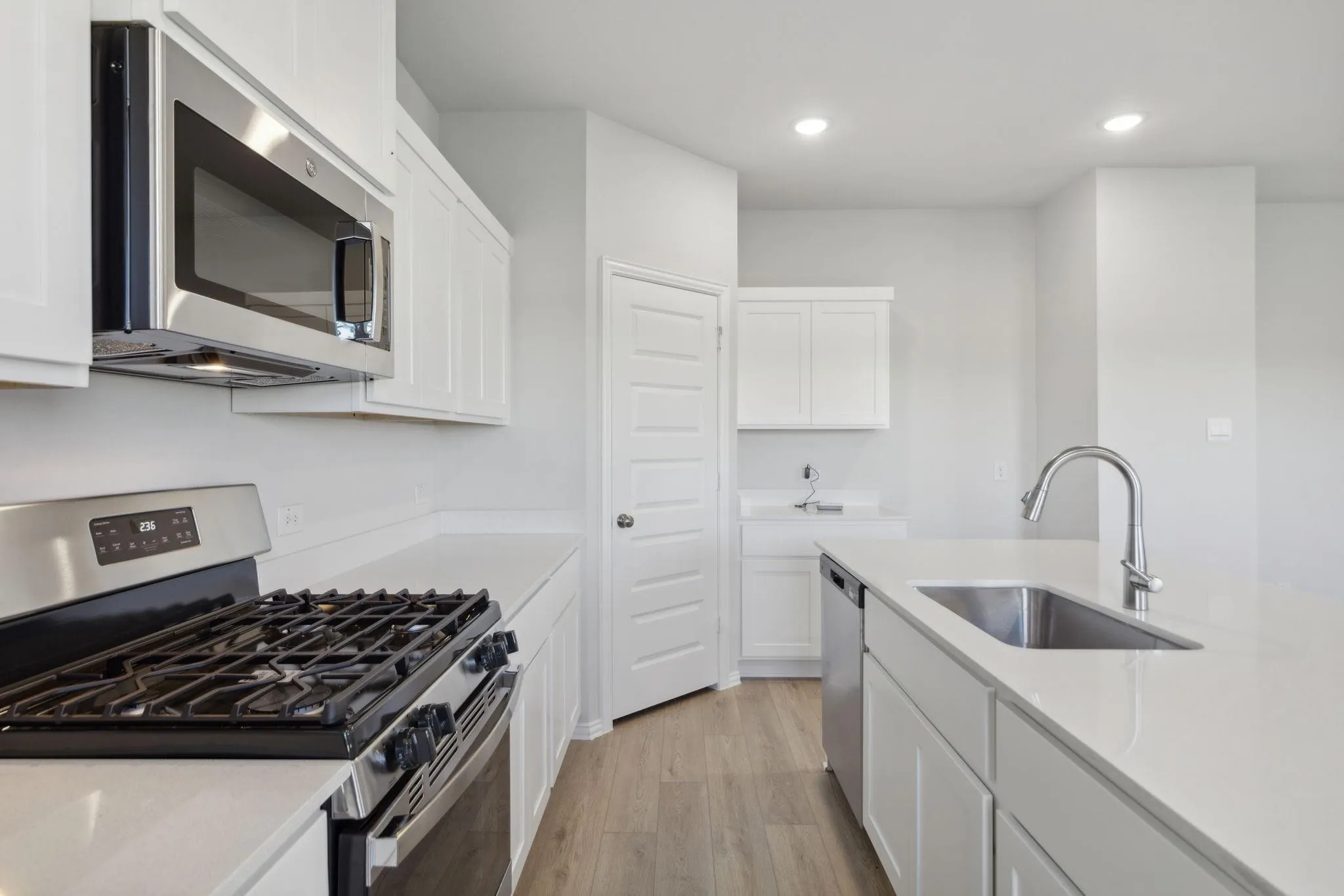 Kitchen with appliances with stainless steel finishes, a sink, light wood-type flooring, white cabinetry, and light countertops
