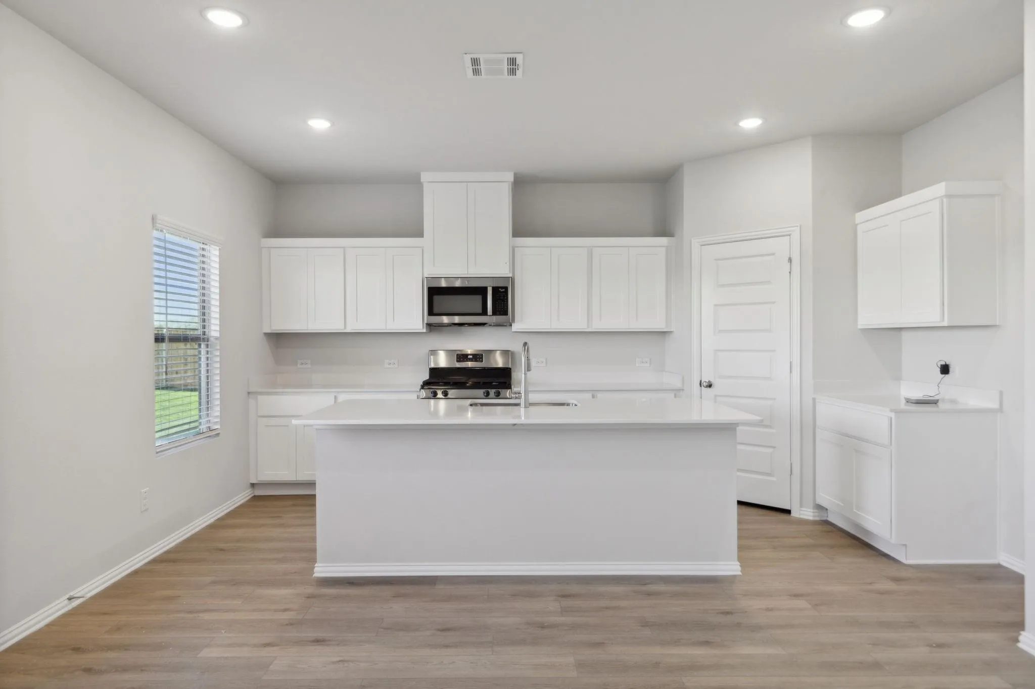 Kitchen with stainless steel appliances, a sink, an island with sink, light countertops, and recessed lighting