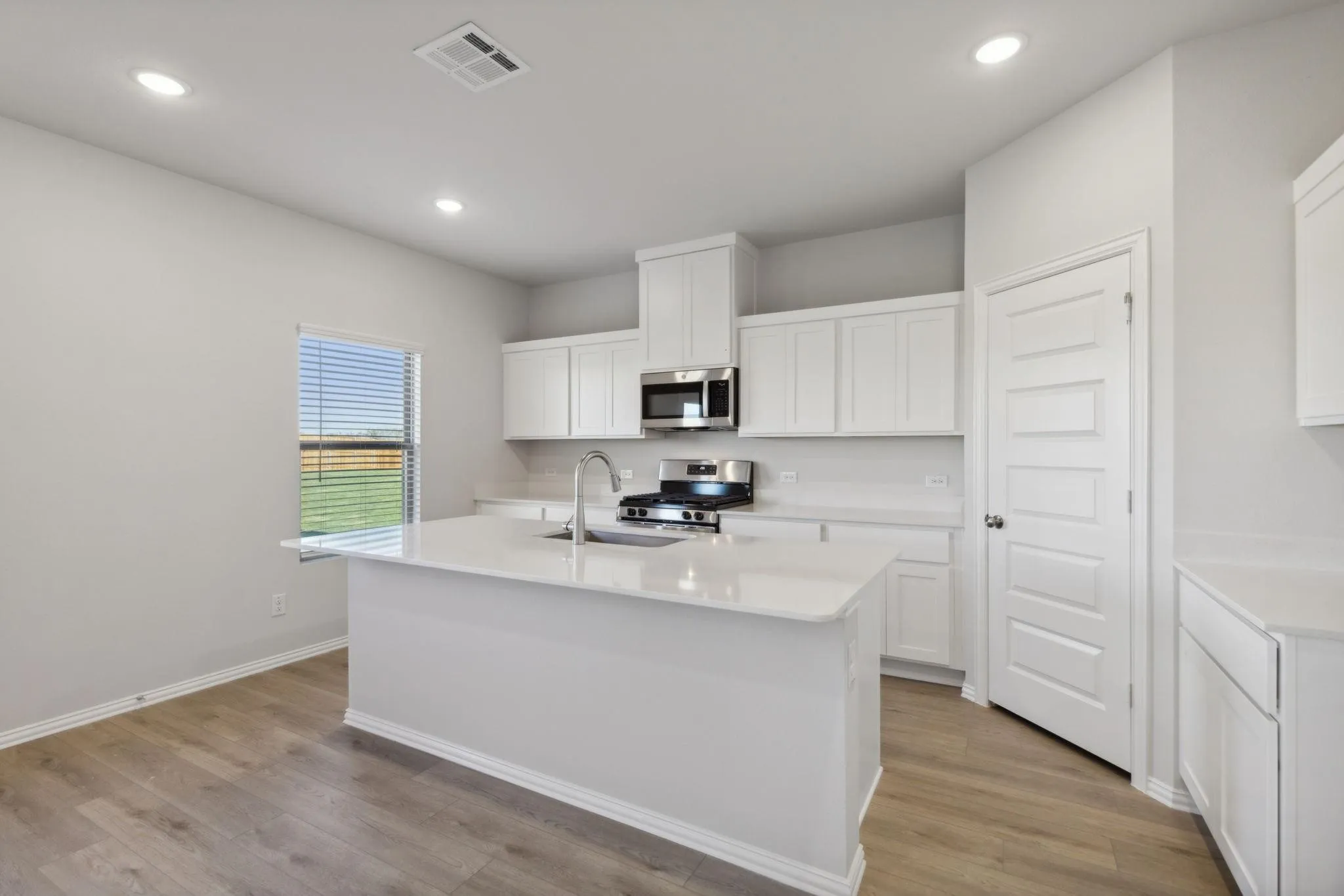 Kitchen with appliances with stainless steel finishes, a sink, light countertops, a center island with sink, and light wood finished floors