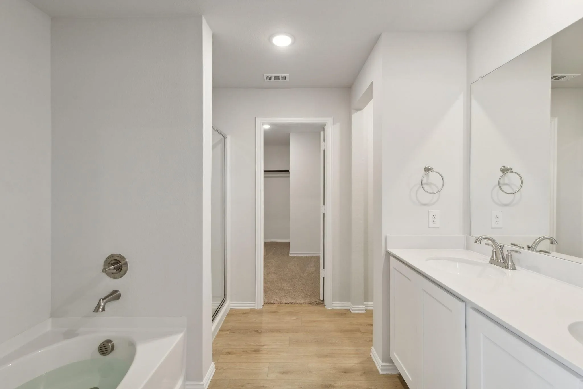 Bathroom featuring a shower stall, wood finished floors, double vanity, a garden tub, and baseboards