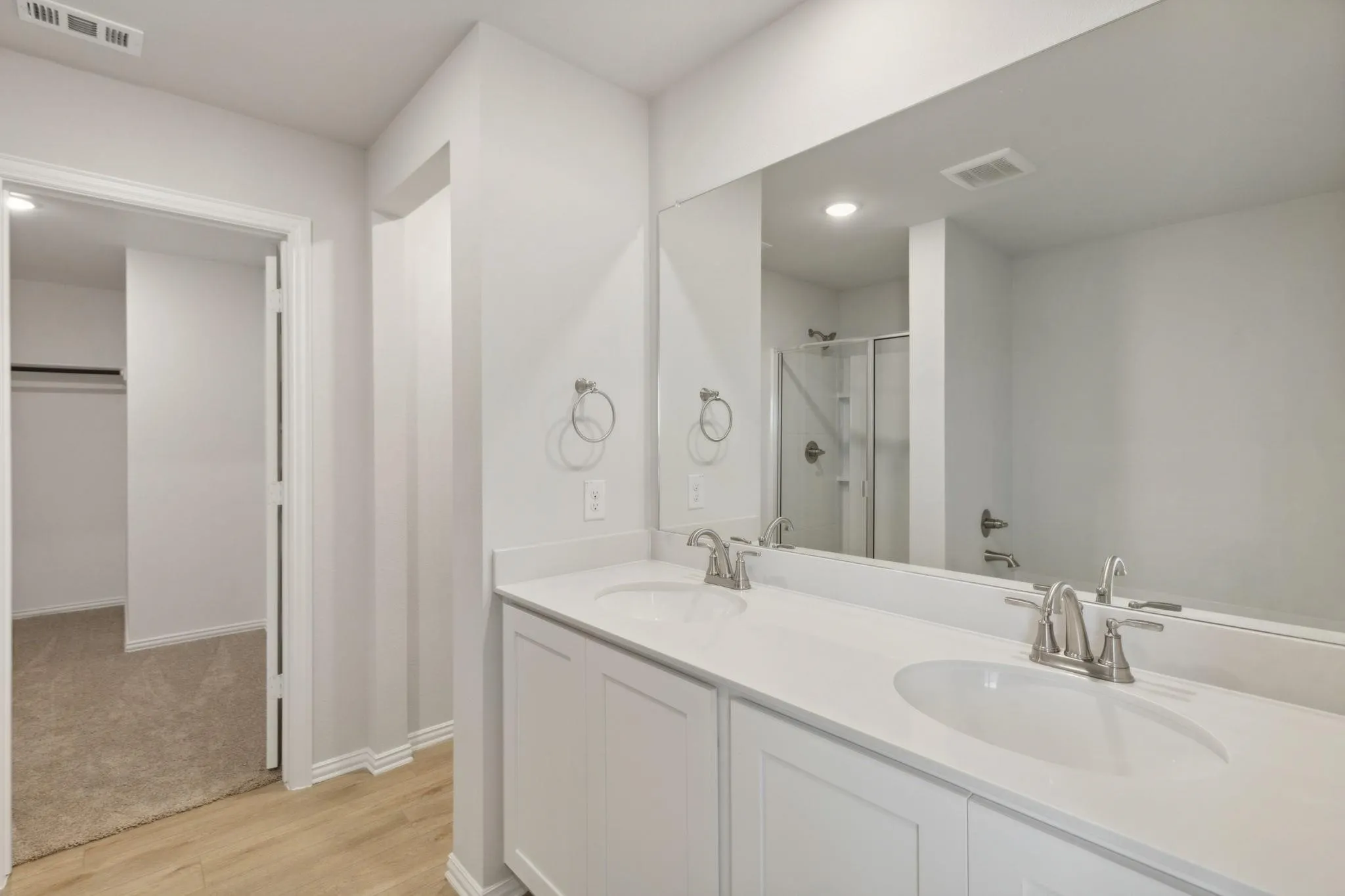 Full bath featuring a shower stall, double vanity, wood finished floors, and baseboards