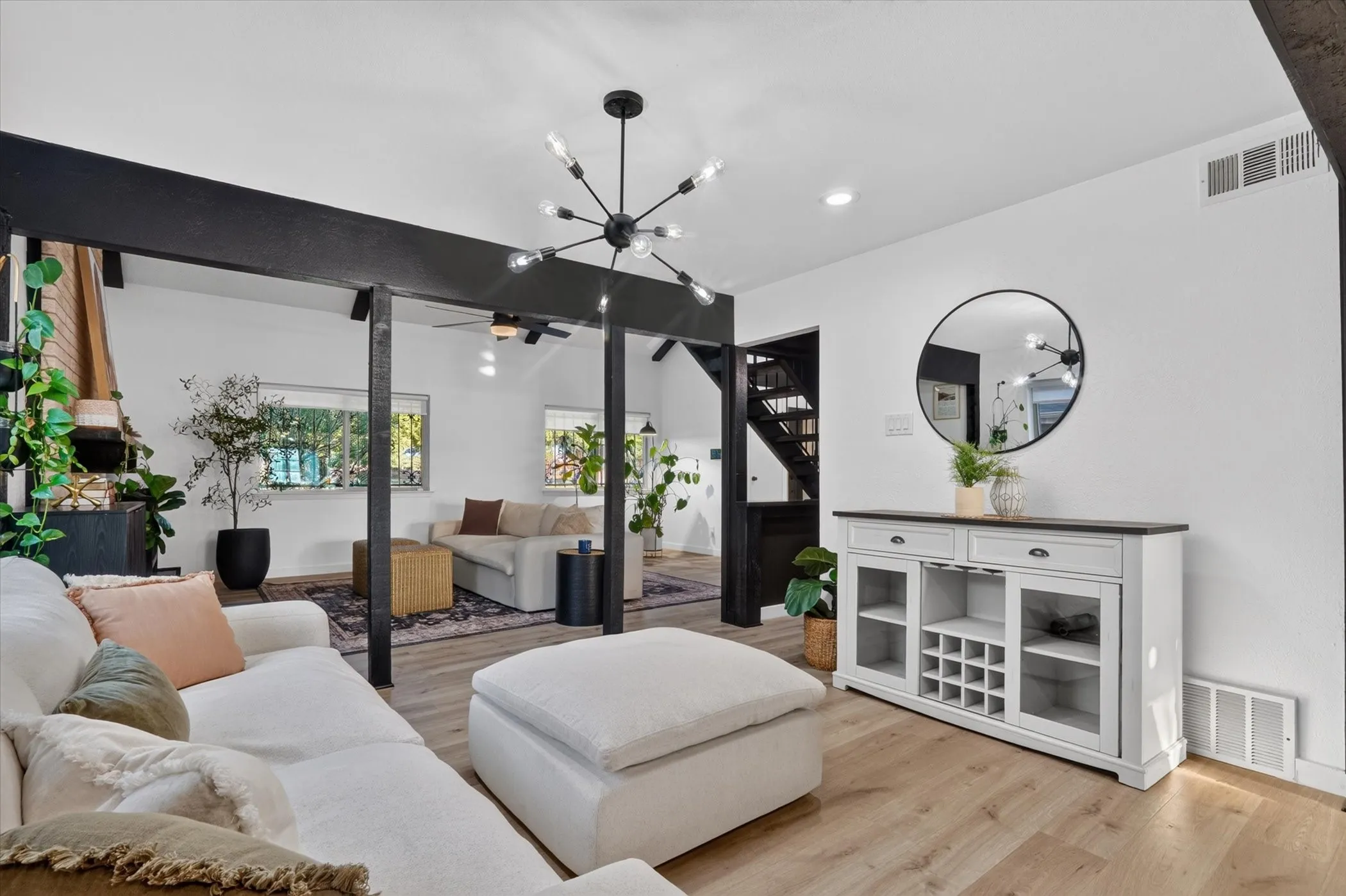 Spacious living area featuring wood-finish flooring, exposed support beams, and a modern chandelier