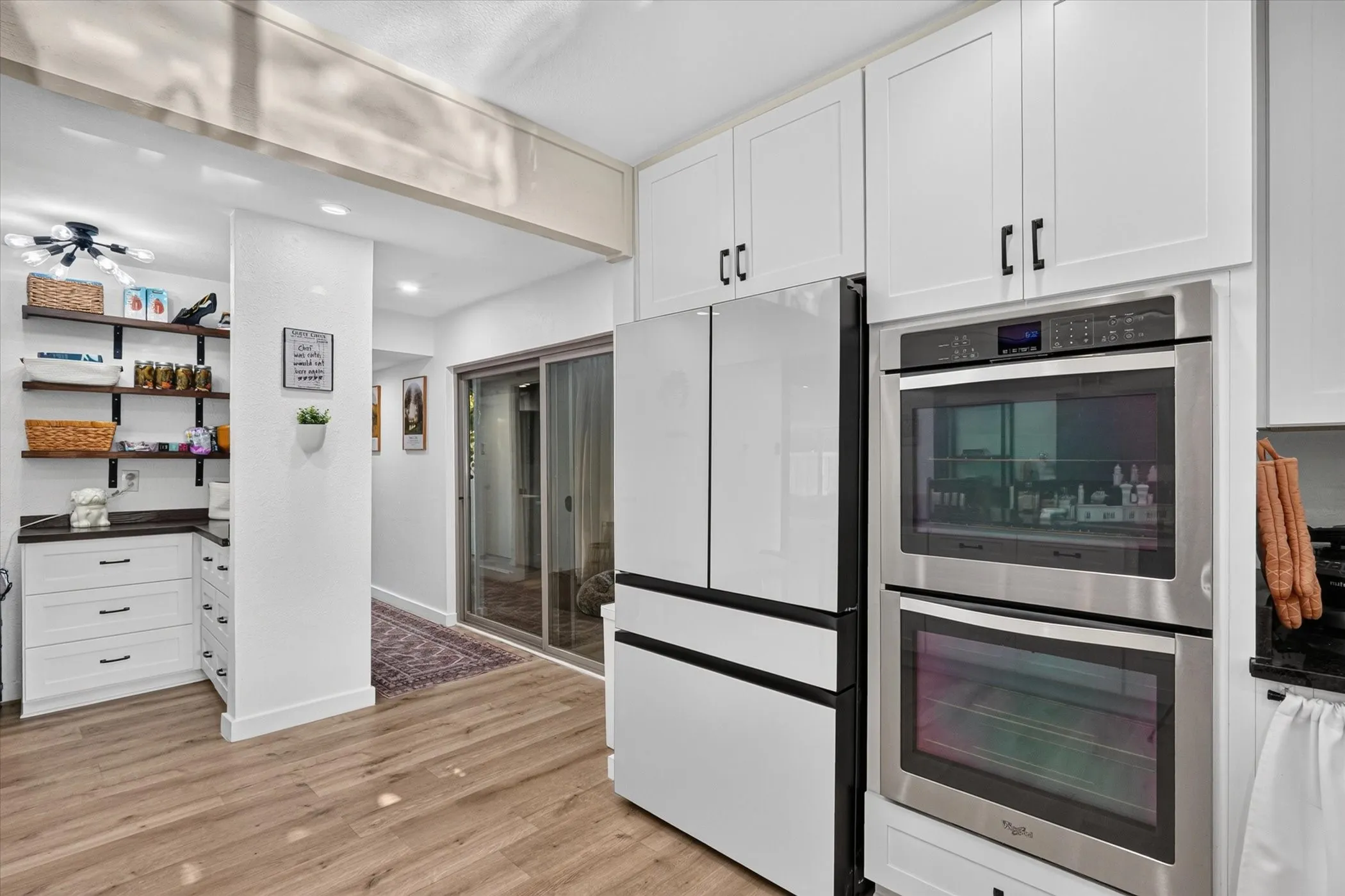 White cabinetry with black hardware, wood-finish flooring, stainless steel double wall oven, and a sliding glass door