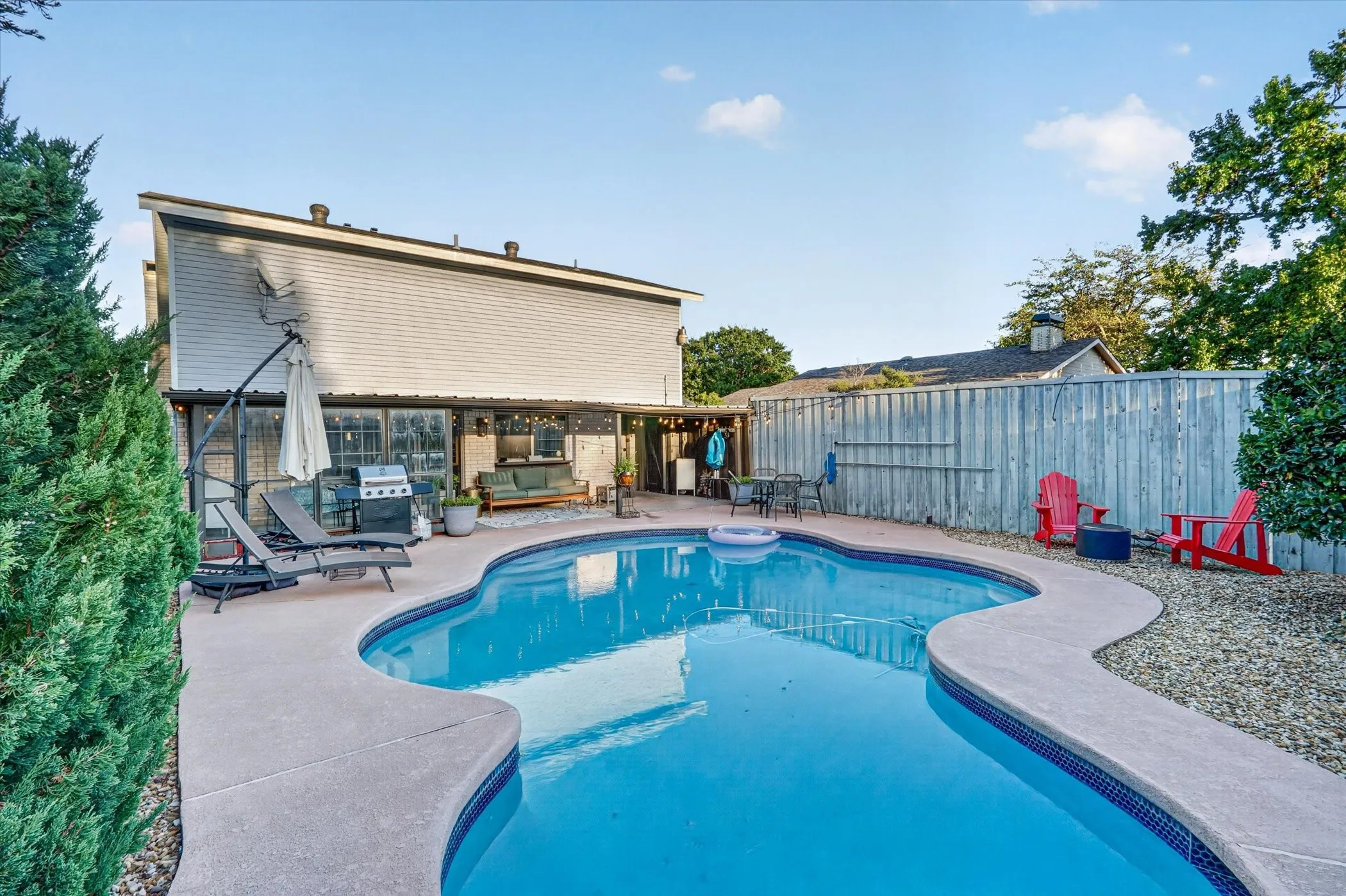 Expansive backyard featuring a freeform swimming pool with a concrete surround, a wood privacy fence, and mature perimeter landscaping
