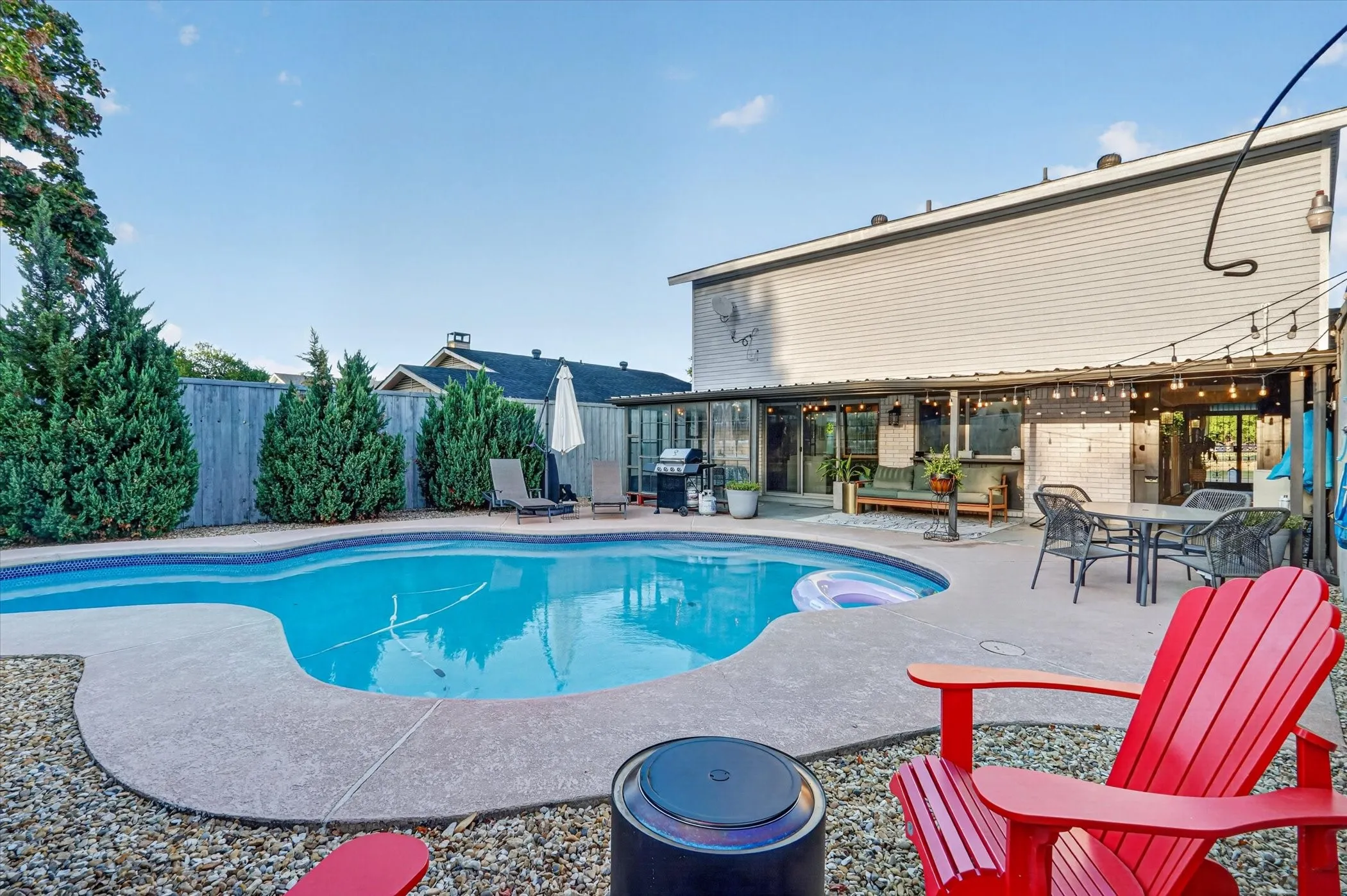 Curved swimming pool, concrete pool deck, covered patio, gravel landscaping, and privacy fencing