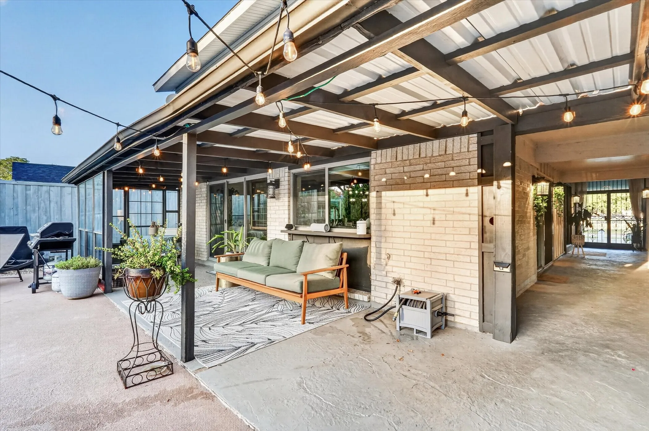 Covered patio featuring string lighting, a white brick exterior, a wood fence, and glass-paneled doors