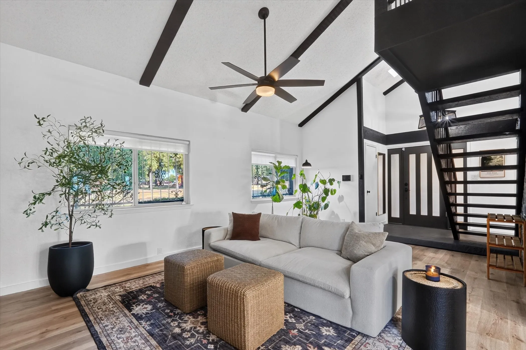 Vaulted ceiling featuring exposed black beams, a contemporary ceiling fan, and wood-finish flooring