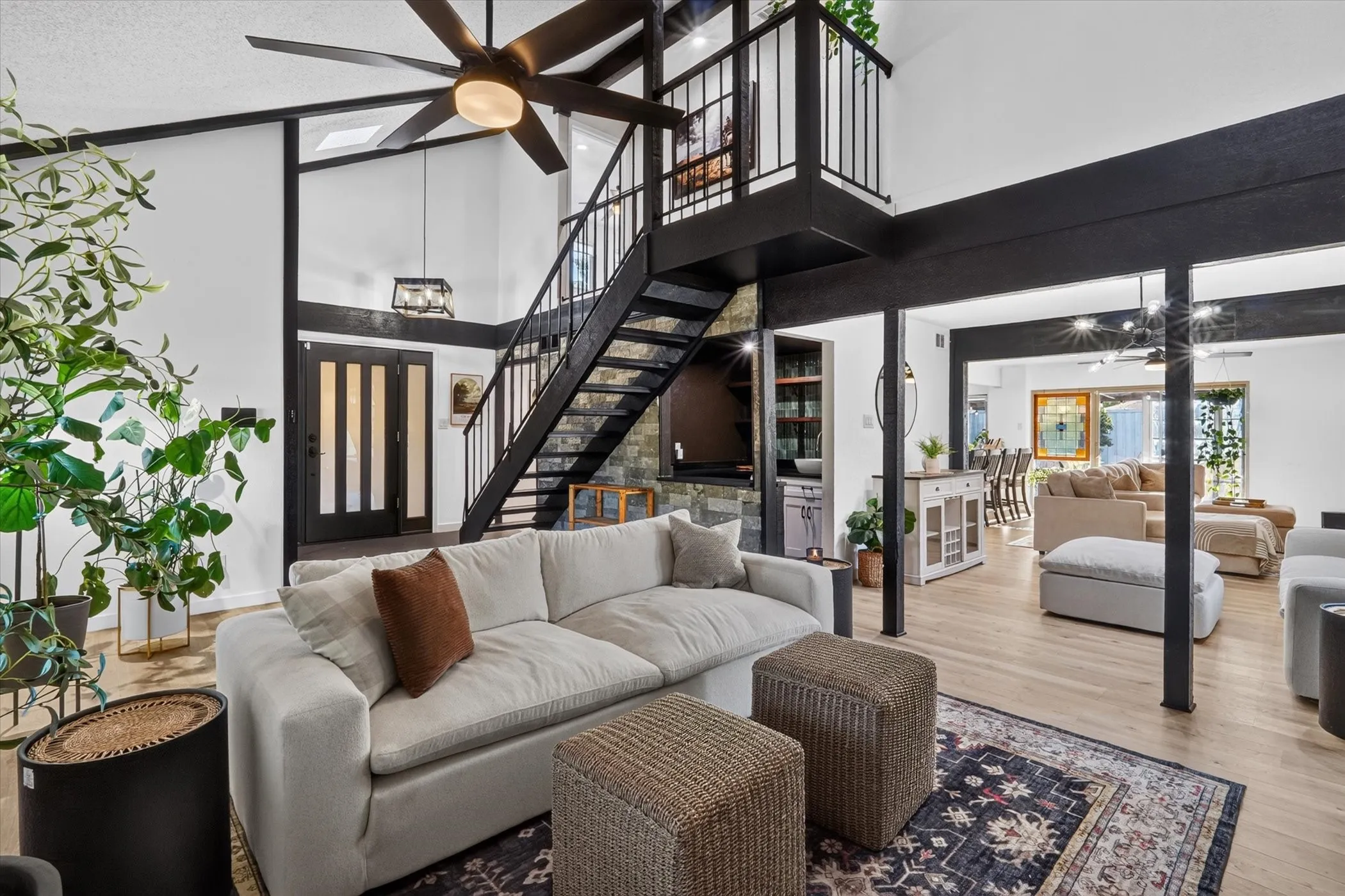 Vaulted ceilings with exposed beams, wood-finish flooring, open tread staircase with metal railing, black frame double doors, and a built-in wet bar