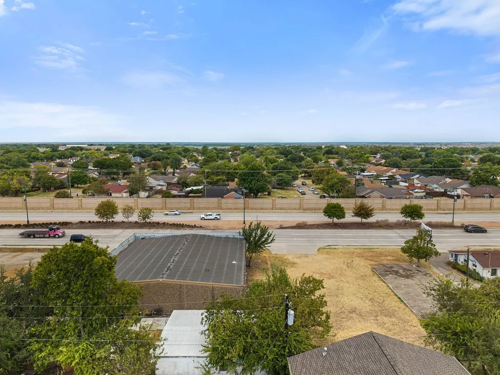 Expansive lot with mature trees, visible paved road access, and surrounding residential structures