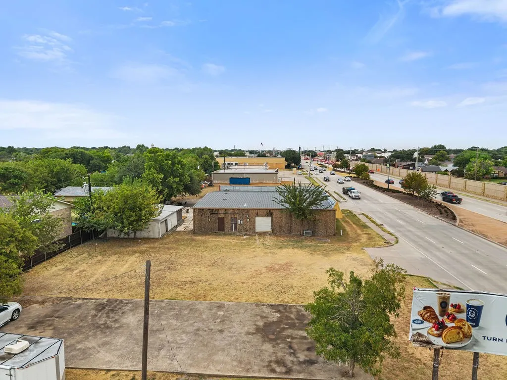 Commercial building with brick exterior and metal roof, situated on a substantial lot with paved and unpaved areas