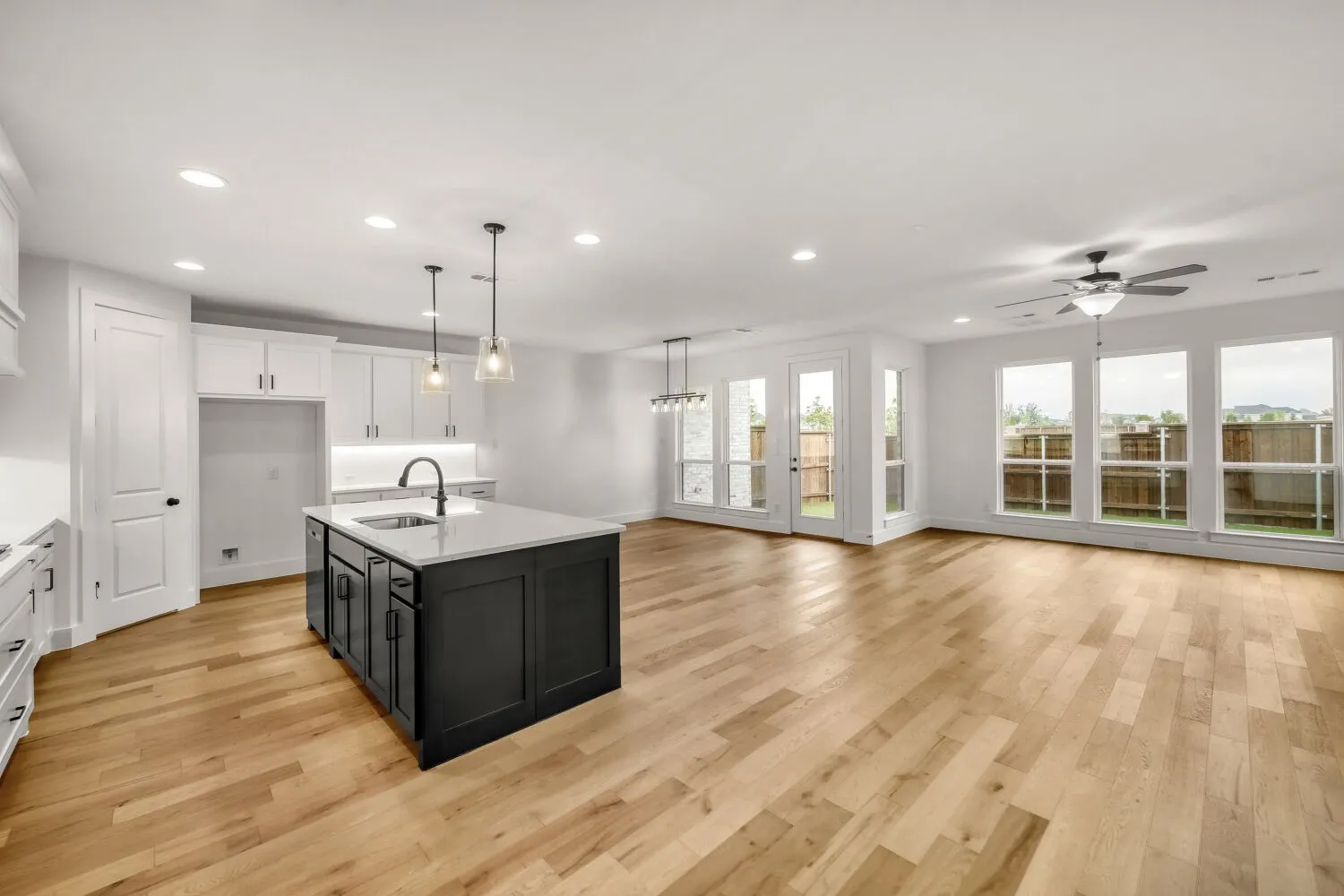 Open concept living space featuring wood-finish flooring, a kitchen island with sink, white shaker cabinetry, recessed lighting, and multiple windows