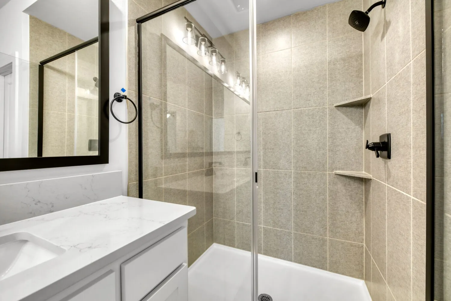 Enclosed shower with full-height tile surround, built-in corner shelving, and matte black fixtures