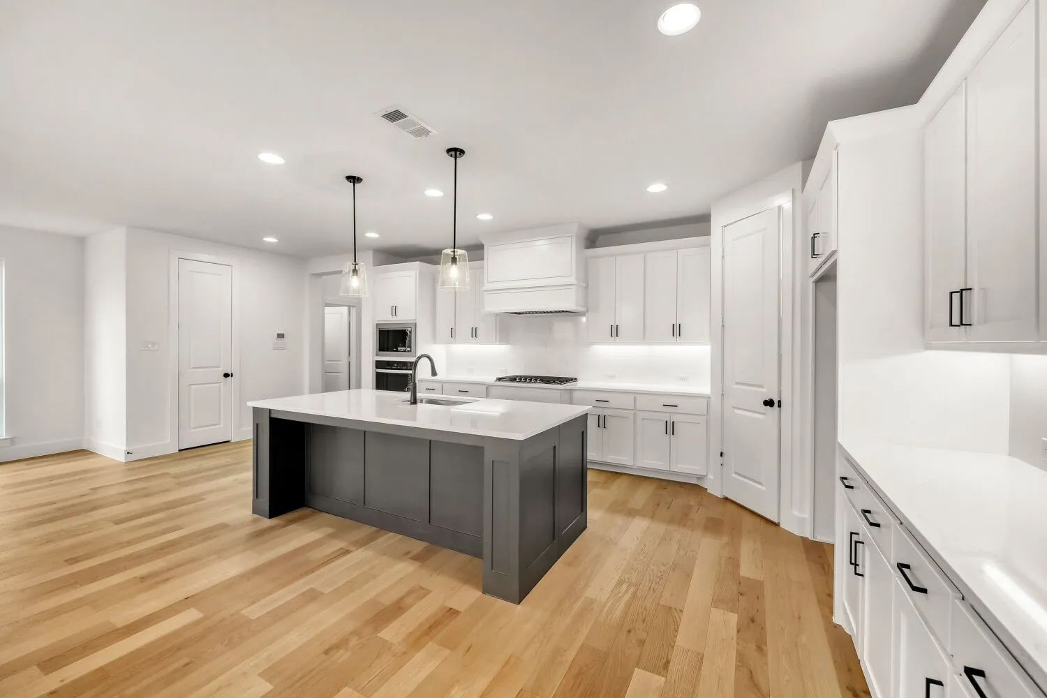 Spacious kitchen featuring an expansive center island, white cabinetry, integrated stainless steel appliances, wood-finish flooring, and recessed lighting