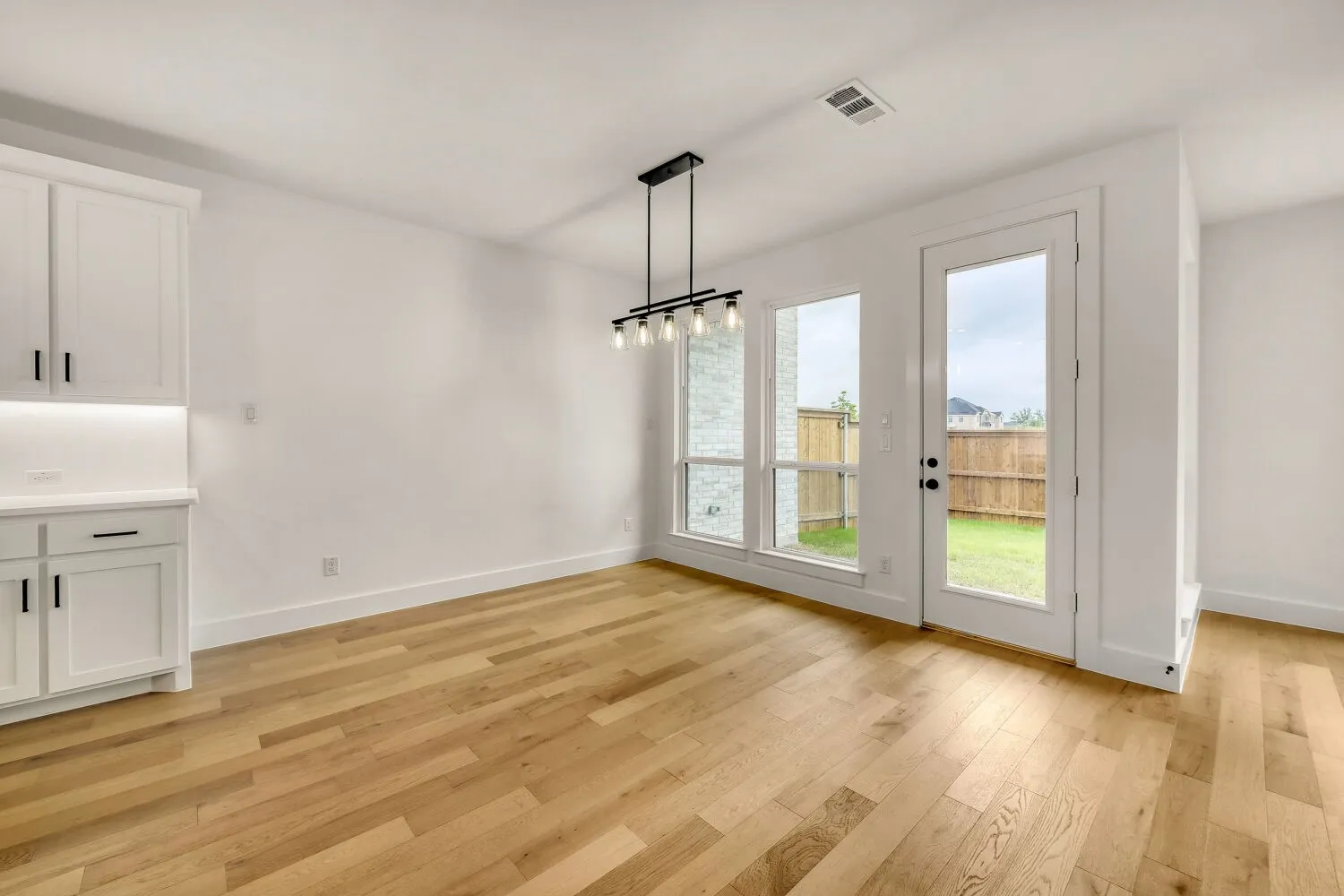 Light wood-finish flooring, built-in cabinetry with undermount lighting, contemporary linear chandelier, glass-paneled exterior door, and a stone accent wall