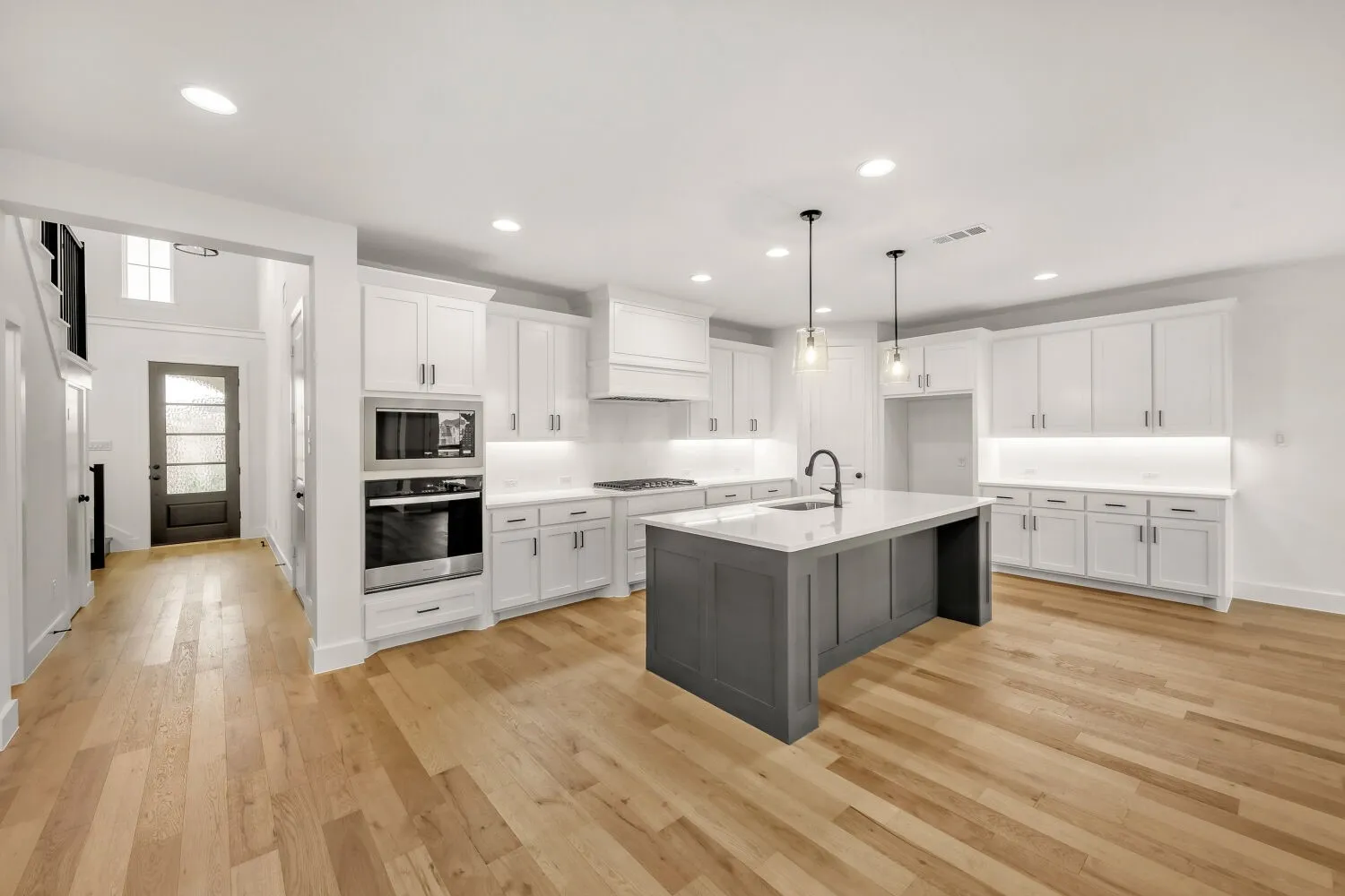 Open-concept kitchen with light wood-finish flooring, white cabinetry, a large kitchen island, and stainless steel built-in appliances