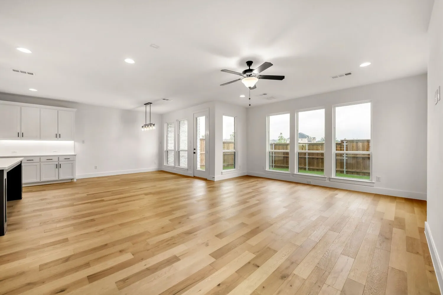 Wood-finish flooring, recessed lighting, white cabinetry, ceiling fan, and multiple large windows