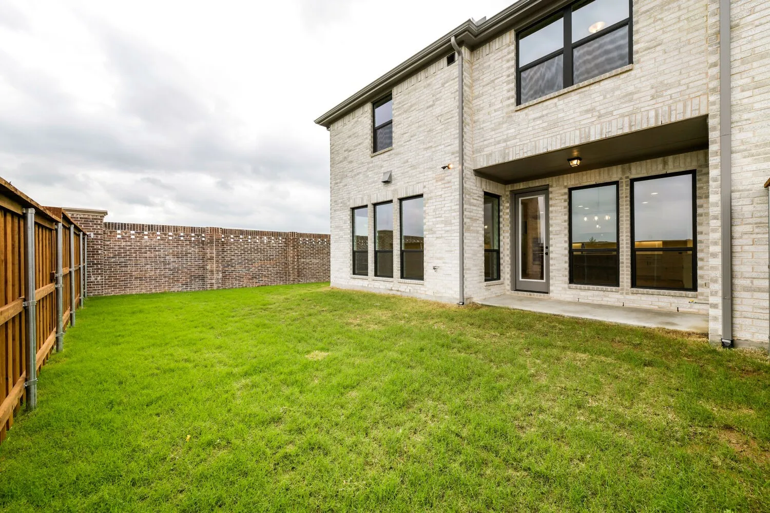 Expansive backyard featuring a manicured lawn, wood privacy fencing, and a brick wall