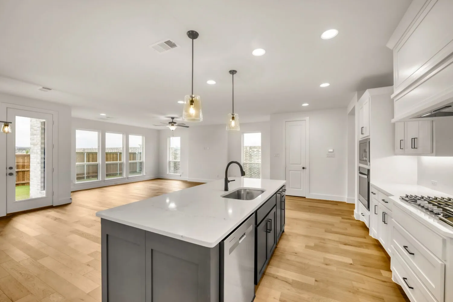 Spacious kitchen and living area featuring a large center island, built-in stainless steel appliances, wood-finish flooring, and recessed lighting