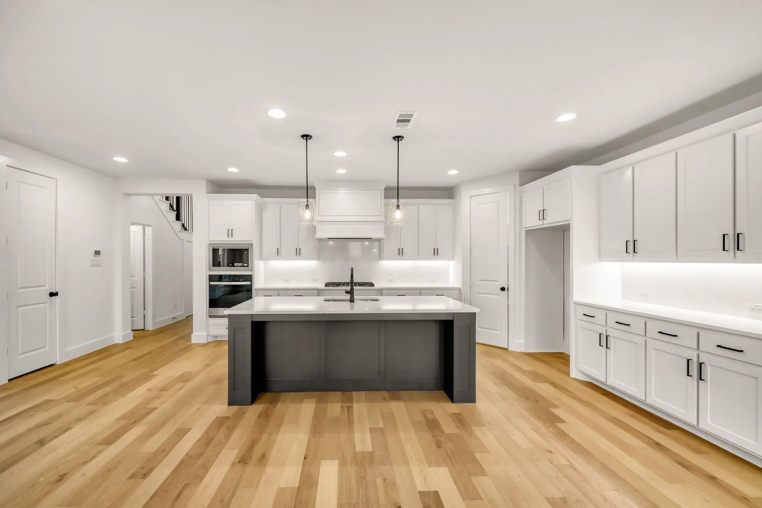 Open-concept kitchen with wood-finish flooring, white cabinetry, a dark-toned island, and recessed lighting