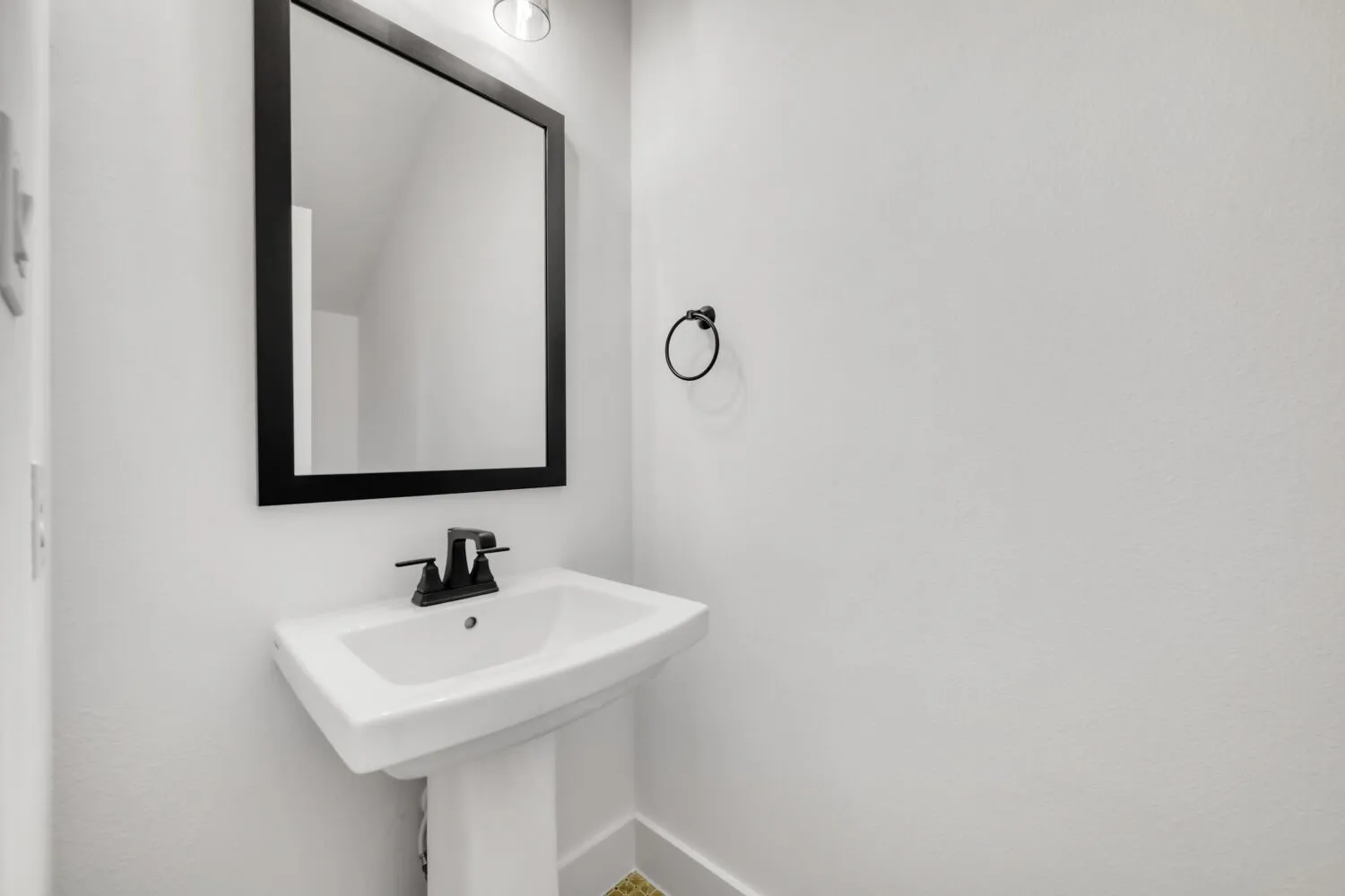 Pedestal sink with matte black faucet, framed mirror, and wall-mounted light fixture