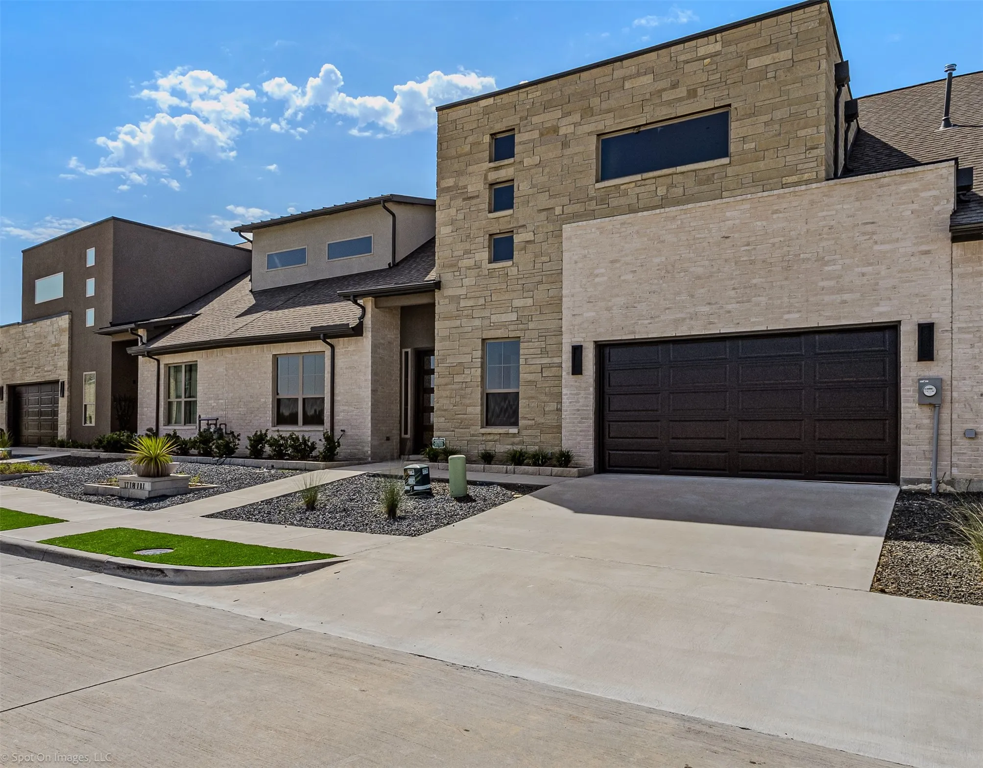 Contemporary exterior featuring stone and stucco finishes, an attached dark panel garage door, a concrete driveway, and low-maintenance landscaping with rock beds