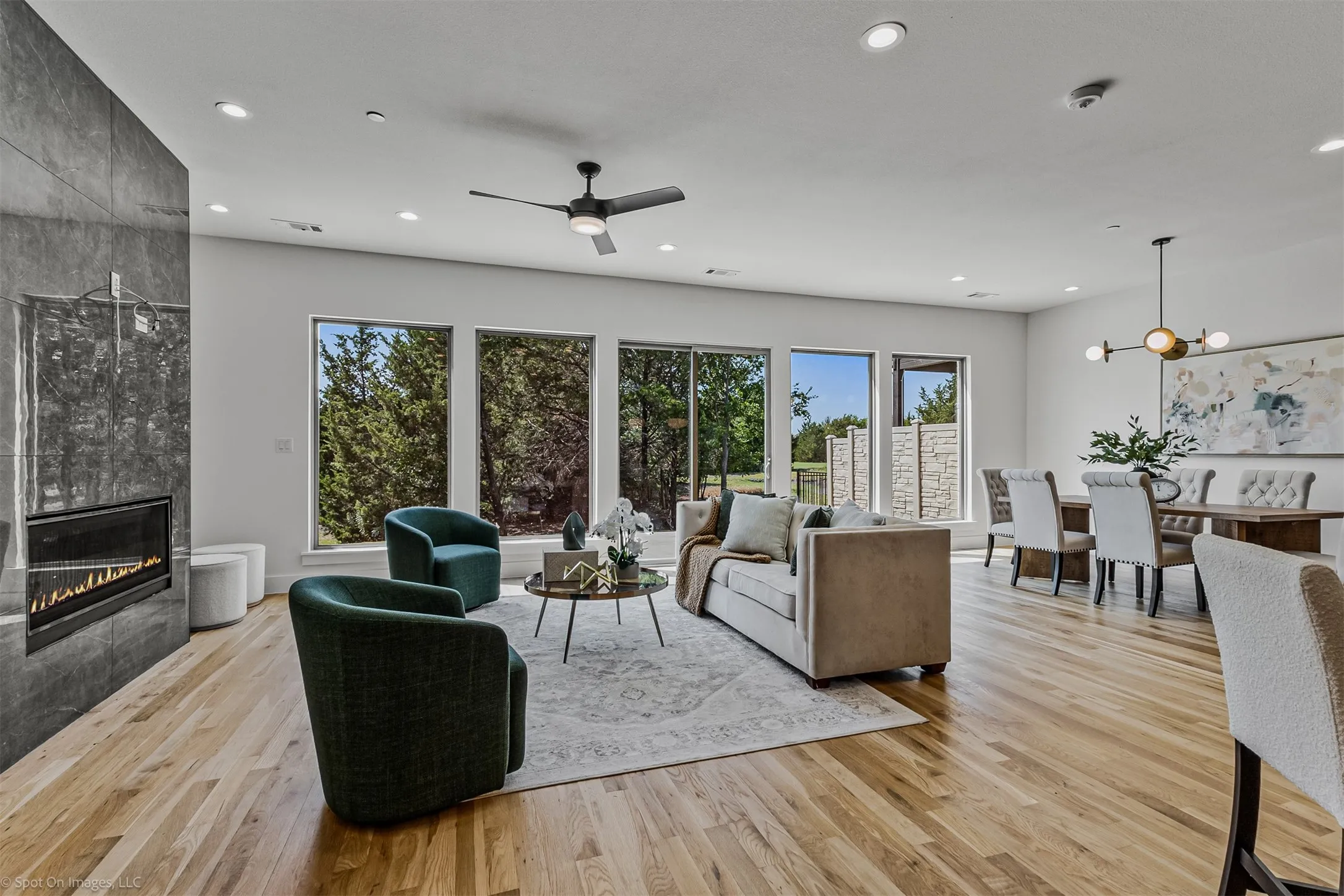 Spacious living area featuring wood-finish flooring, an integrated linear fireplace with a stone surround, and large windows