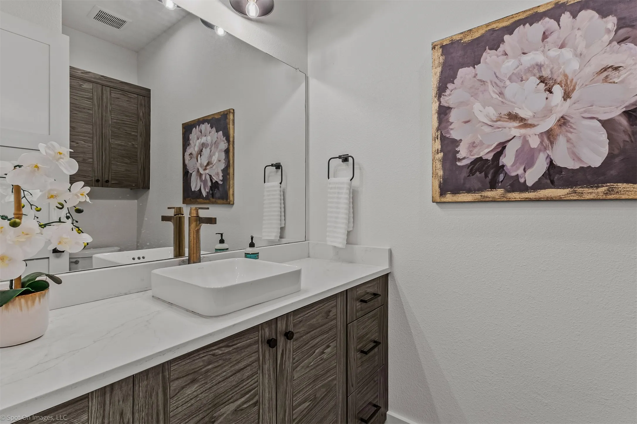 Floating rectangular vessel sink, white countertop, wood-finish cabinetry, bronze-finish fixtures, and a large wall mirror