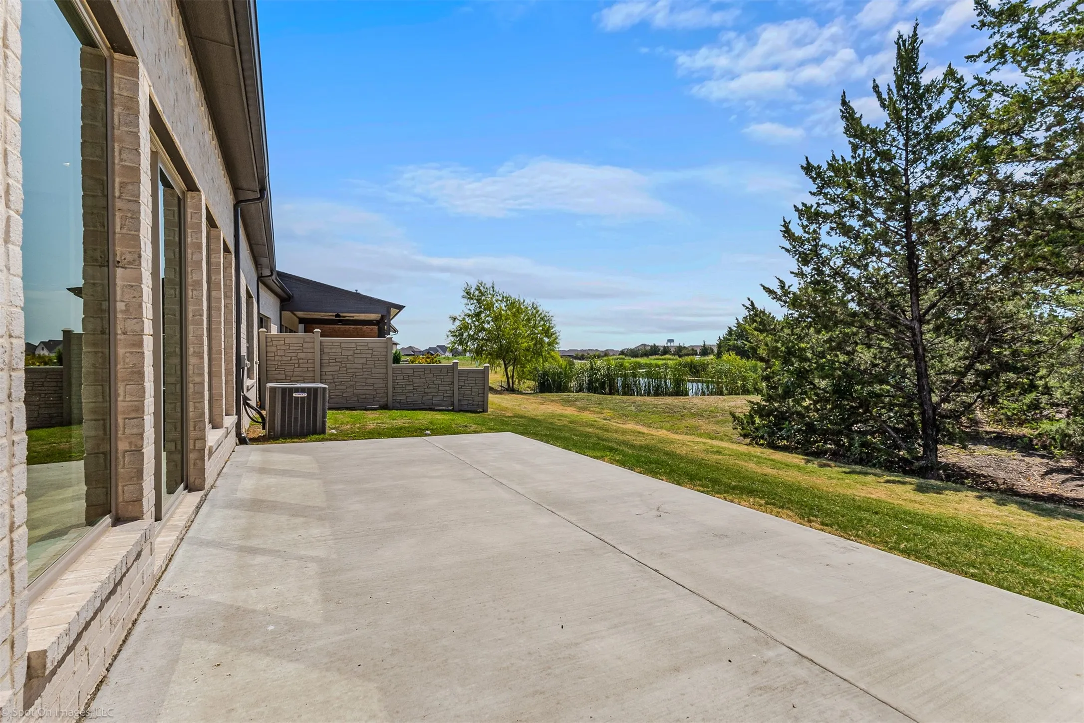 Concrete patio with a brick exterior, expansive windows, and mature trees bordering a body of water