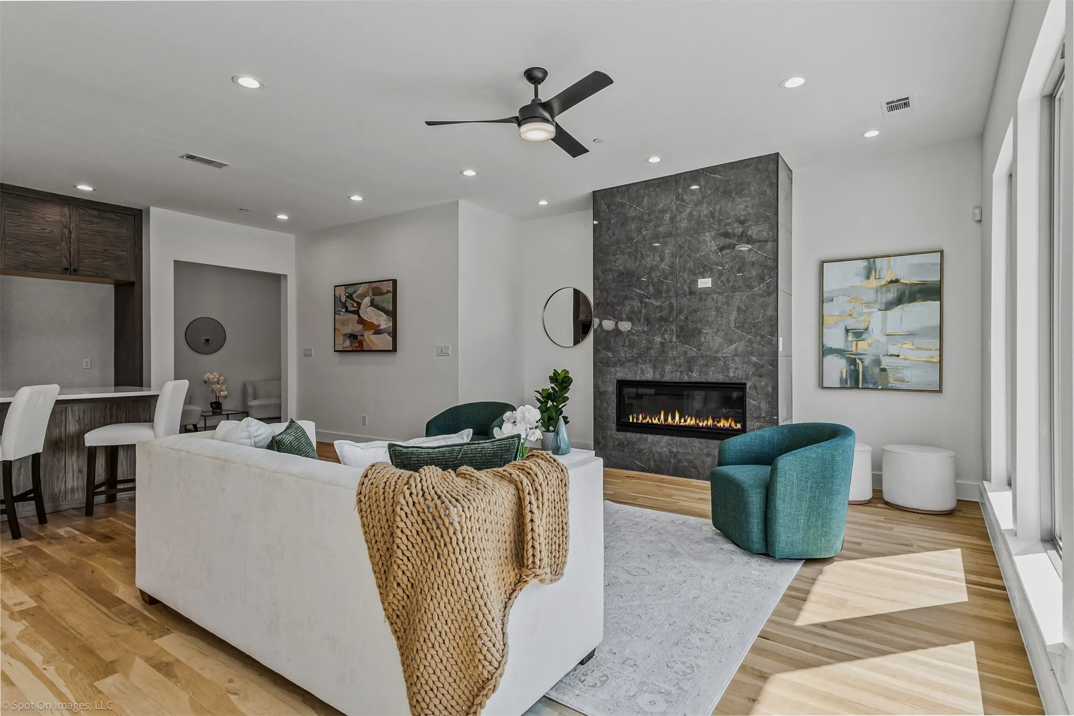 Hardwood-style flooring throughout, a modern fireplace with a dark stone surround, recessed lighting, and a ceiling fan