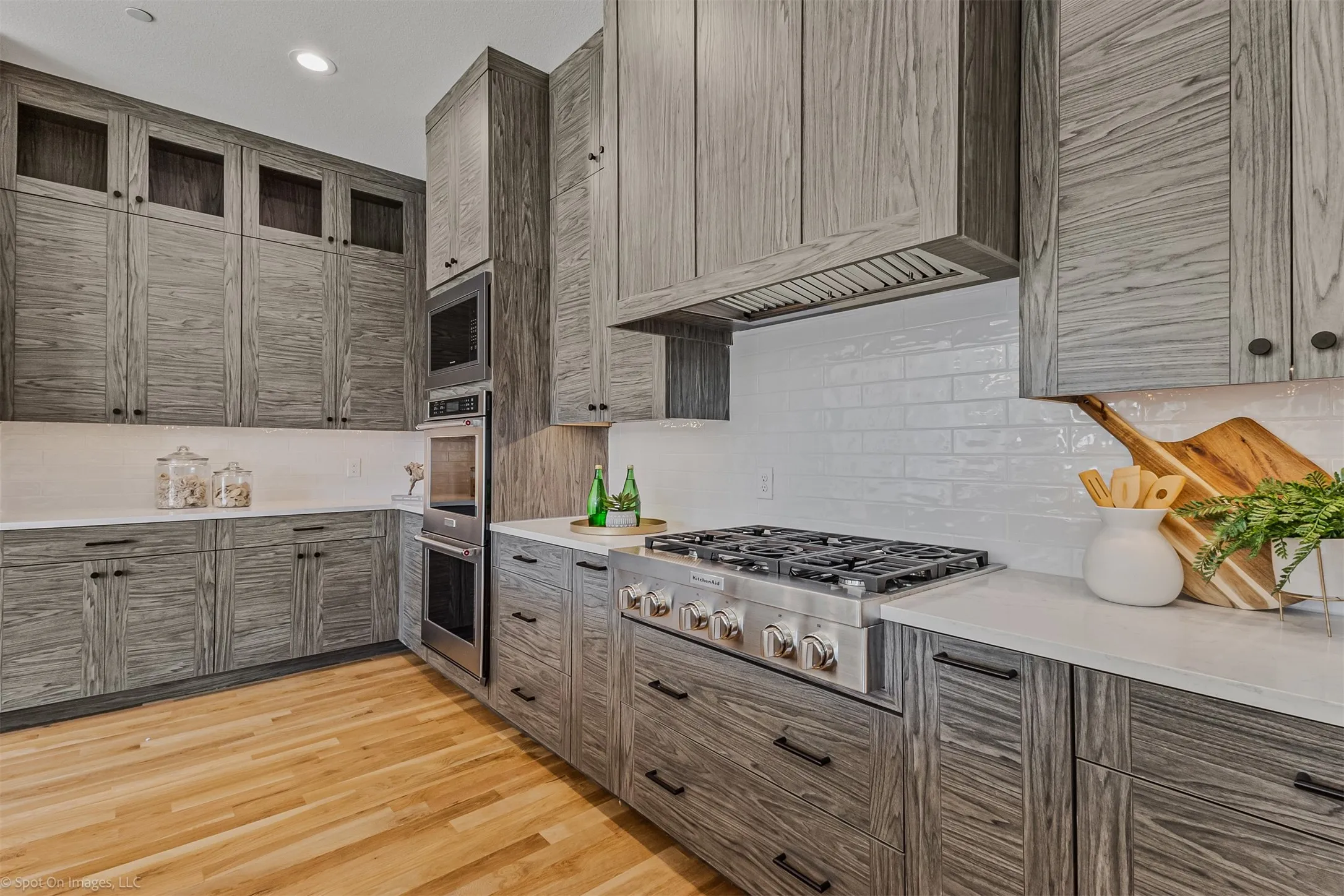 Wood-finish cabinetry, stainless steel gas range, integrated stainless steel double oven, subway tile backsplash, and light-toned countertops