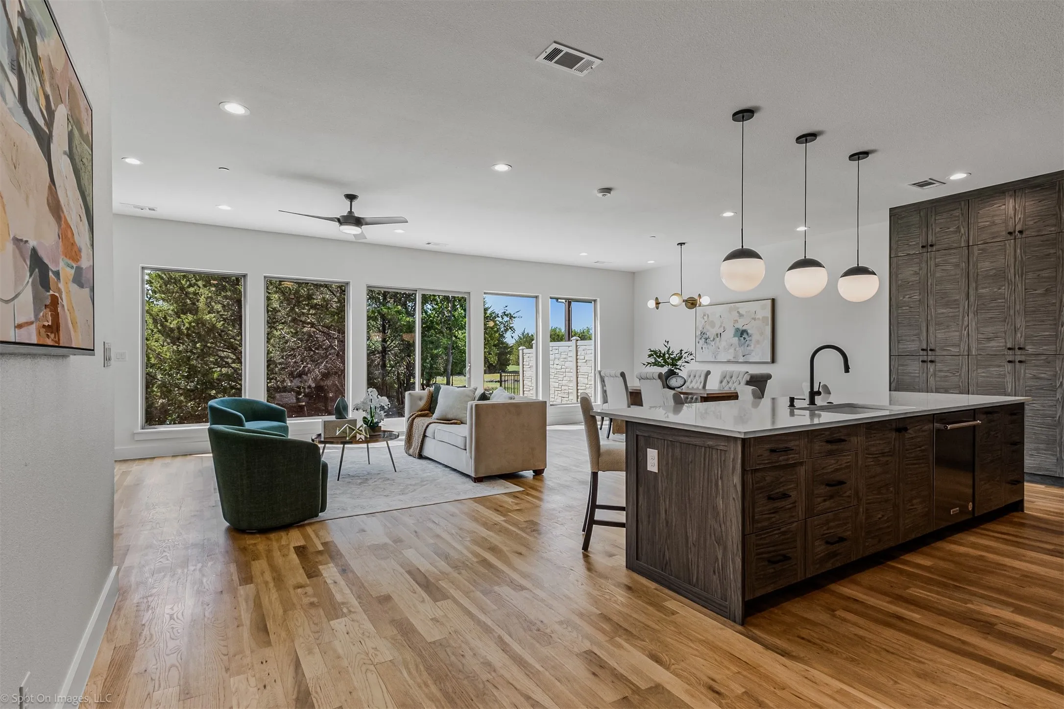 Open-concept living space with hardwood flooring, a kitchen island featuring a sink and dishwasher, pendant lighting, and recessed ceiling lights