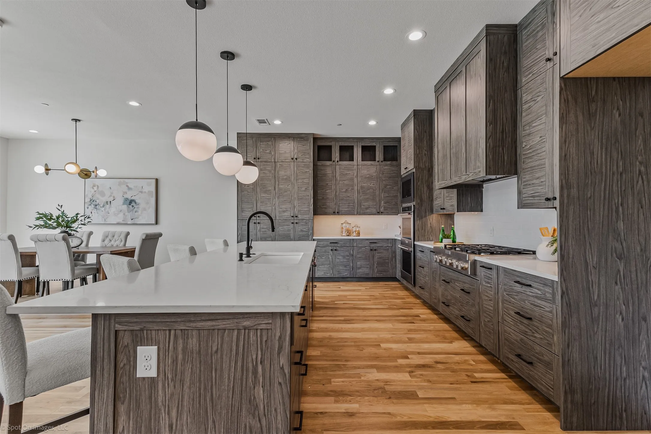 Expansive kitchen featuring wood-finish cabinetry, built-in stainless steel appliances, a center island with a sink, and pendant lighting