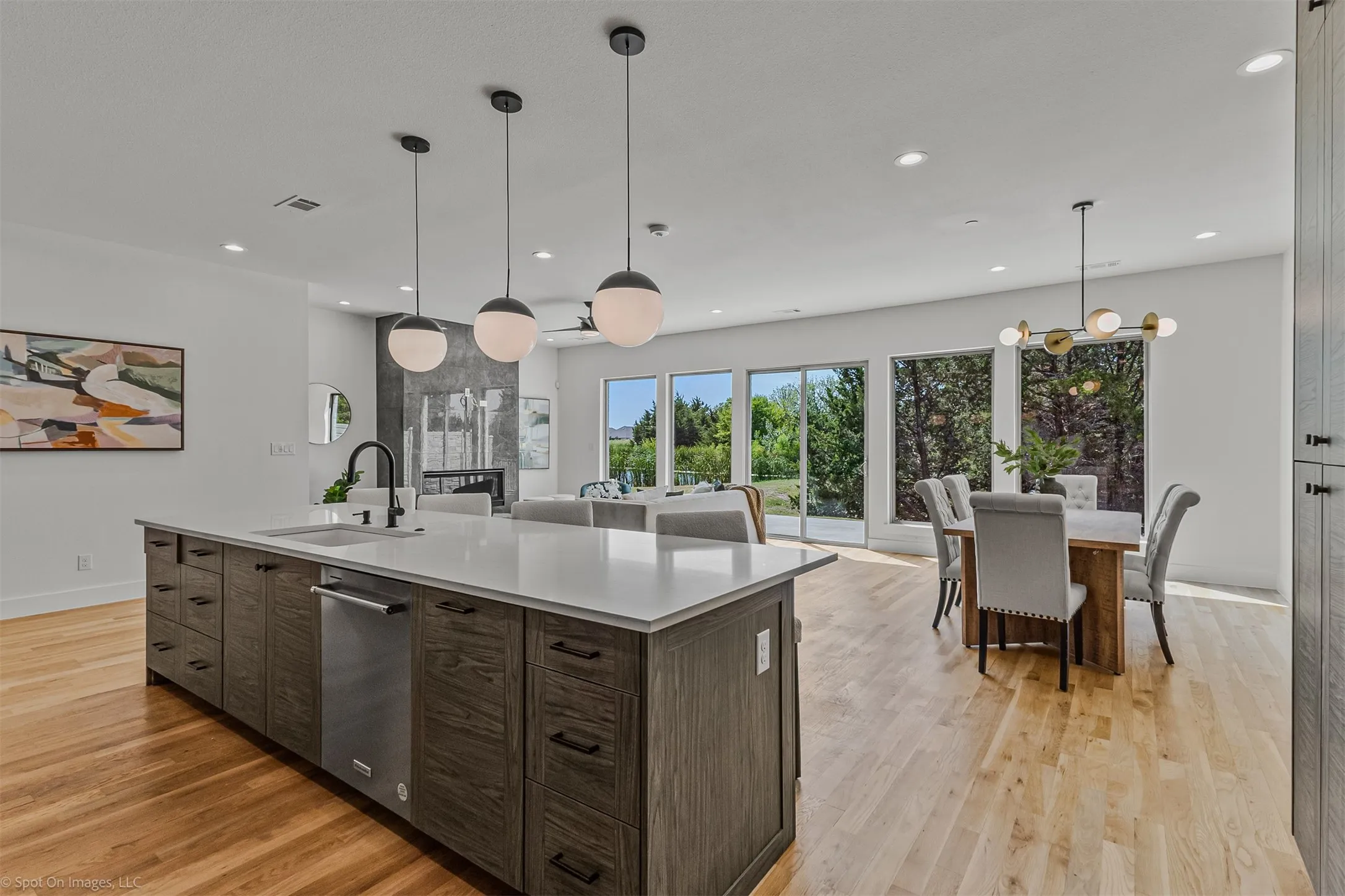 Open-concept living space with light wood-finish flooring, a large kitchen island with integrated sink, recessed lighting, and expansive windows