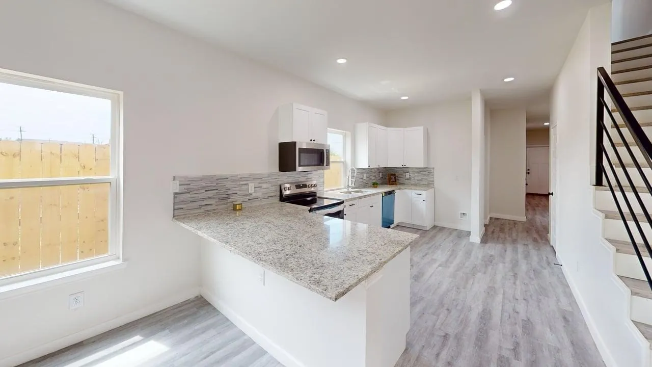 Modern kitchen featuring white cabinetry, light-toned countertops, a tile backsplash, and stainless steel appliances