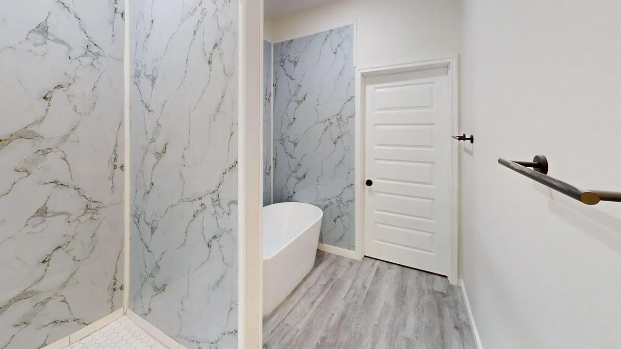 Freestanding soaking tub, wood-finish flooring, and a white paneled door