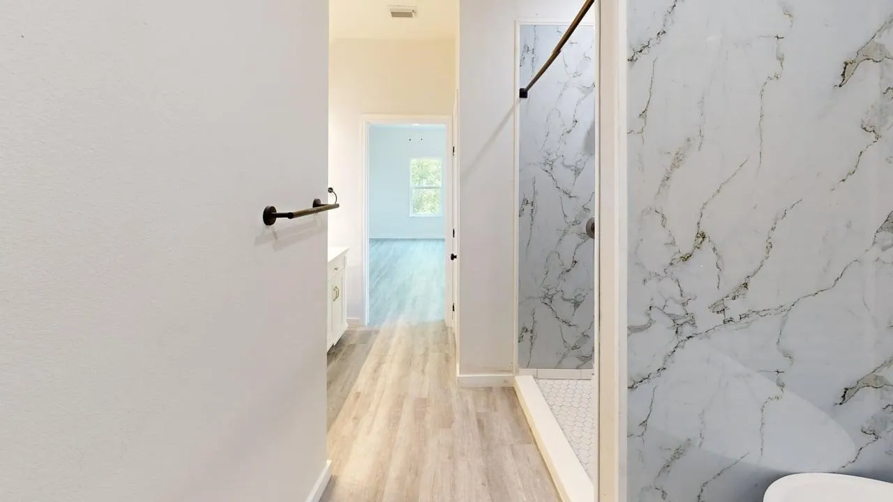Shower with a white marble-look surround, hexagonal tile floor, and dark bronze fixtures
