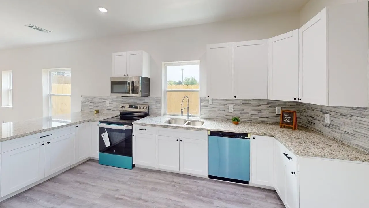 White shaker-style cabinetry with black hardware, stainless steel sink, light-toned backsplash, and light-toned countertops
