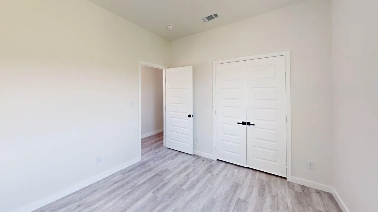 Light-toned wood-finish flooring, white walls, and a white paneled bi-fold closet door with black hardware