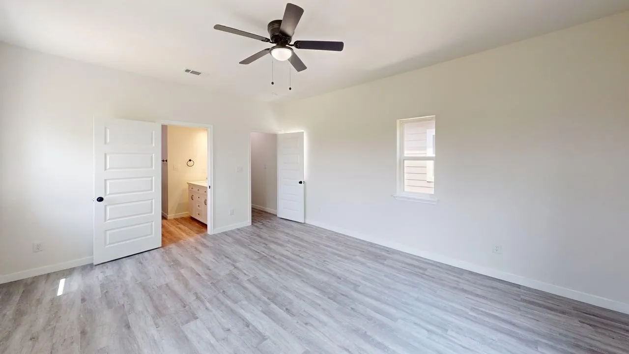Spacious room featuring wood-finish flooring, a ceiling fan with integrated lighting, and white paneled doors