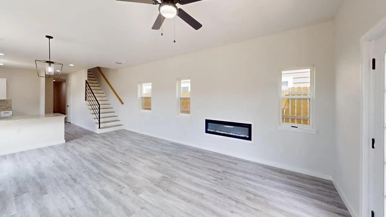 Wood-finish flooring, built-in electric fireplace, contemporary ceiling fan, modern geometric chandelier, and open staircase with metal railing