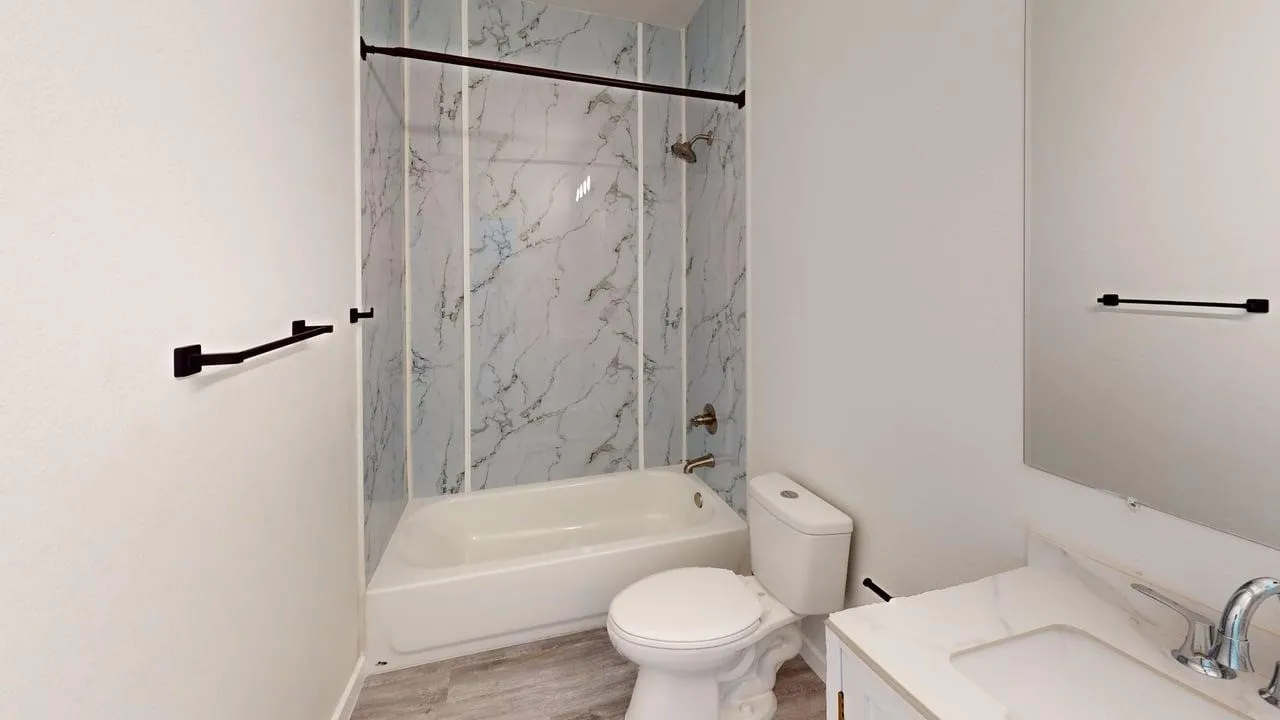 Bathroom featuring a bathtub with a shower, marble-patterned surround, wood-finish flooring, and a vanity with a rectangular sink