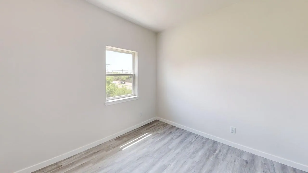 Wood-finish flooring with white baseboards and a single window offering natural illumination