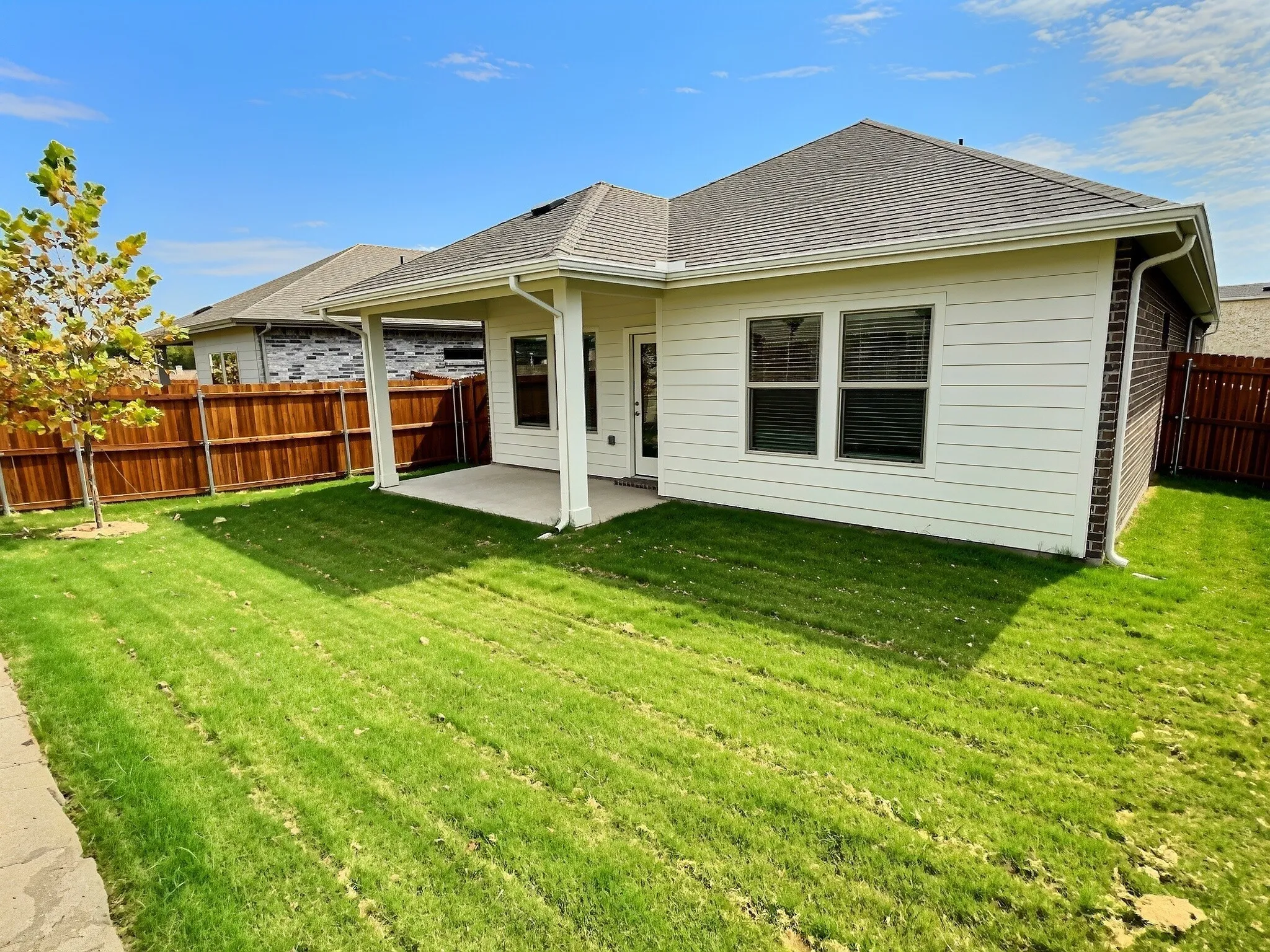 Expansive backyard featuring a covered patio, privacy fencing, and a manicured lawn