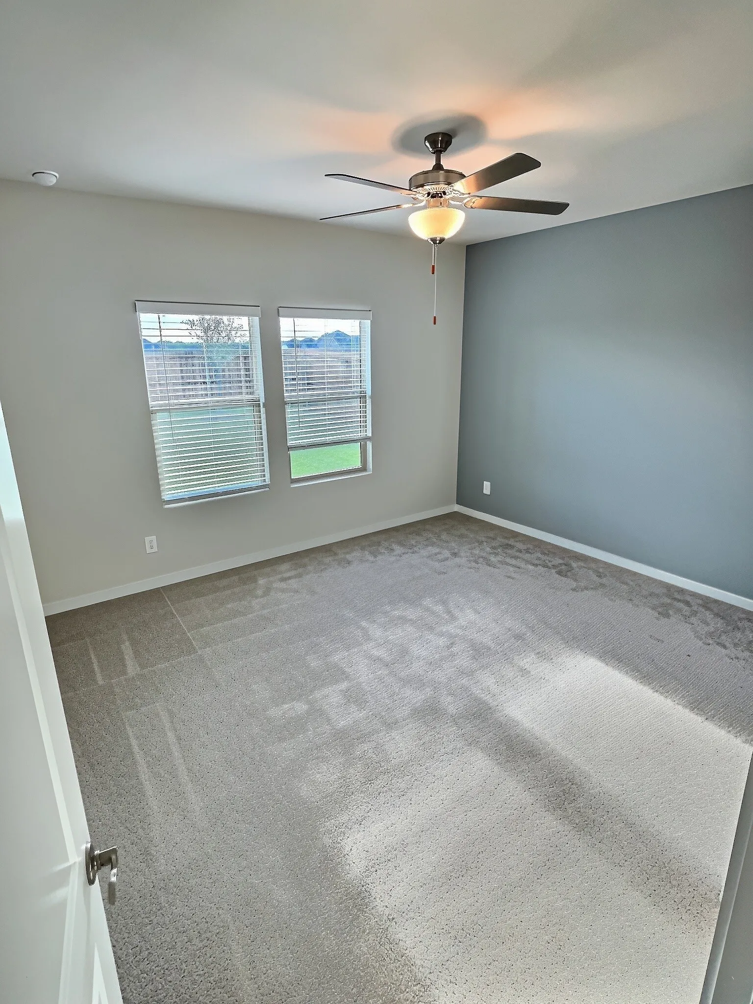 Plush carpeting, dual windows with blinds, ceiling fan with integrated lighting, and a neutral wall palette