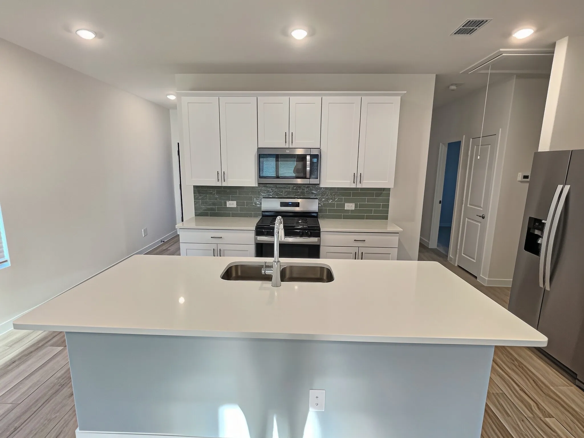 Kitchen featuring a spacious island with an undermount sink, stainless steel appliances, white cabinetry, and a subway tile backsplash