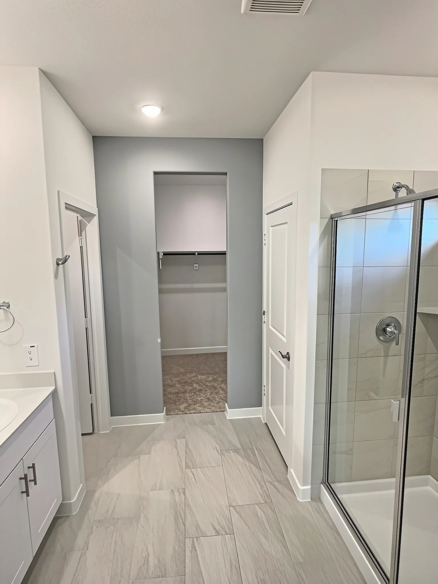 Spacious bathroom featuring large format tile flooring, a walk-in shower with glass enclosure, and a vanity with a white countertop