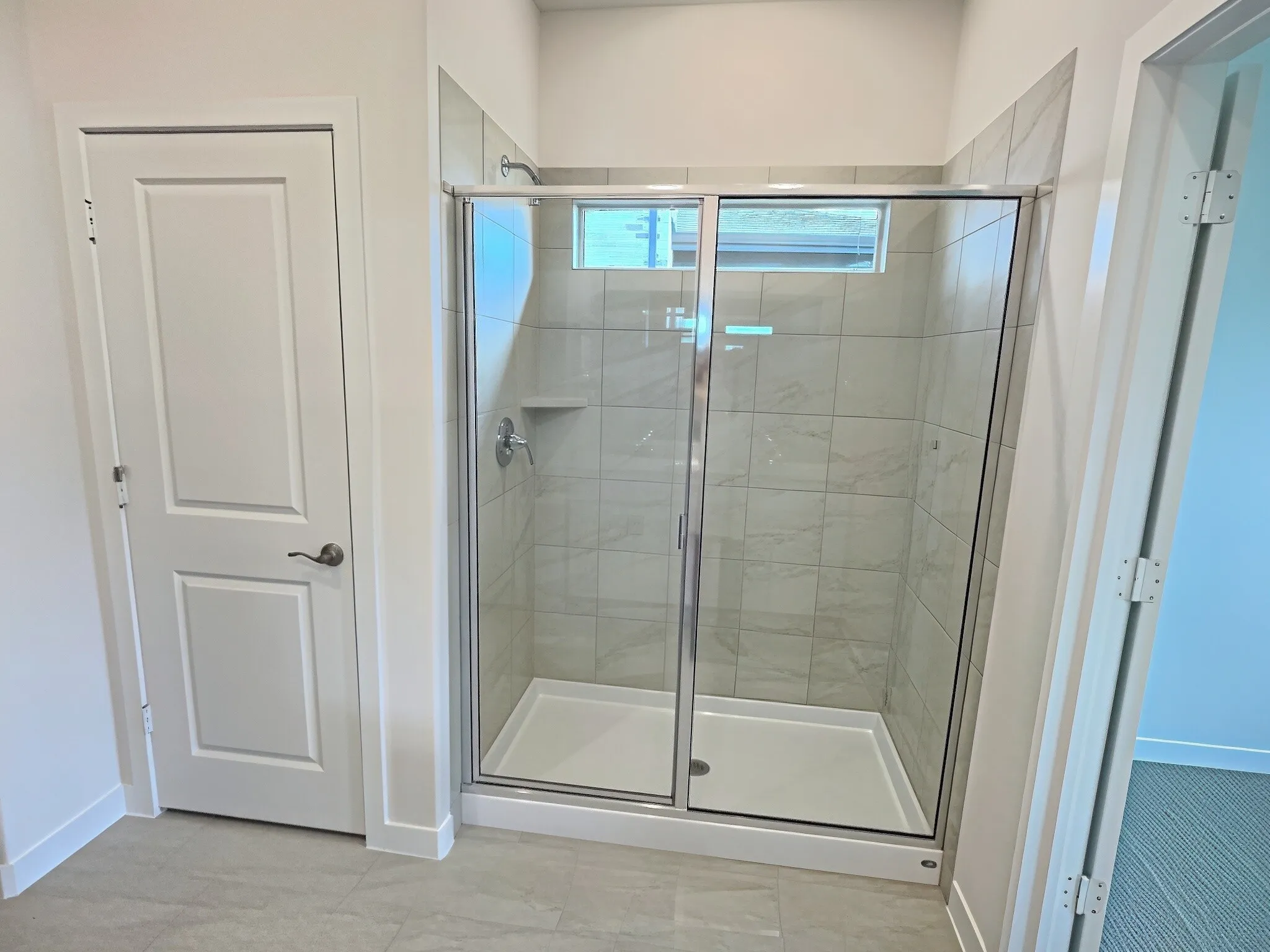 Glass-enclosed shower with tile surround, built-in shelving, and a transcom window