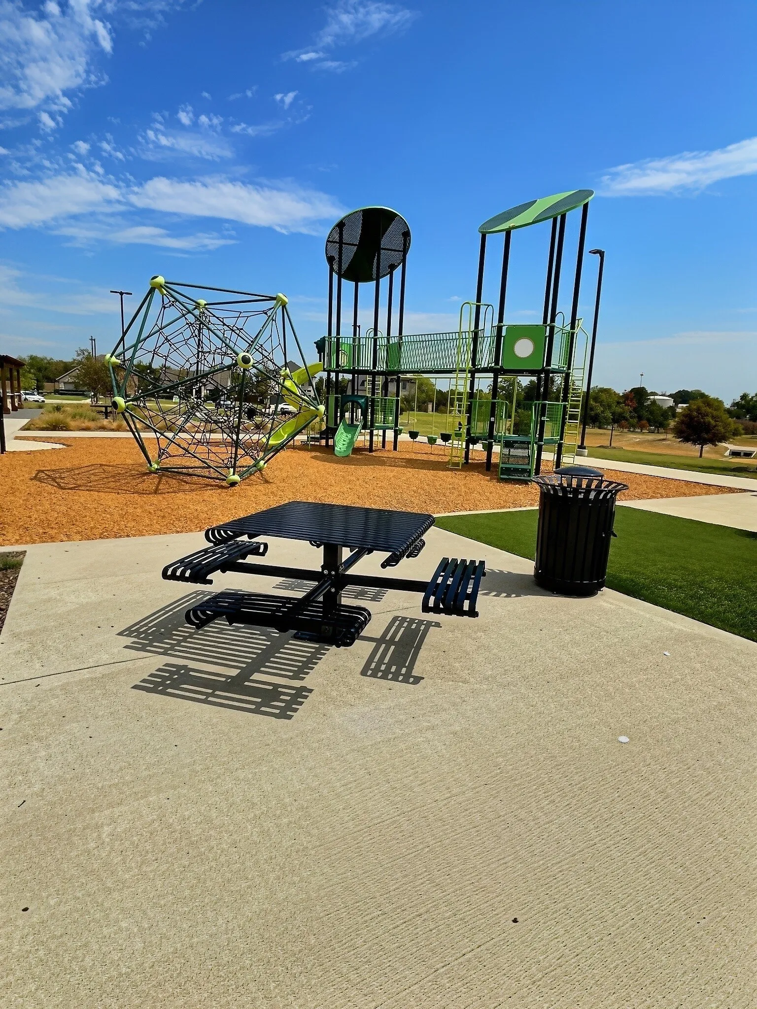 Recreational area featuring a climbing structure, multi-level playground equipment, a picnic table, and concrete pathways