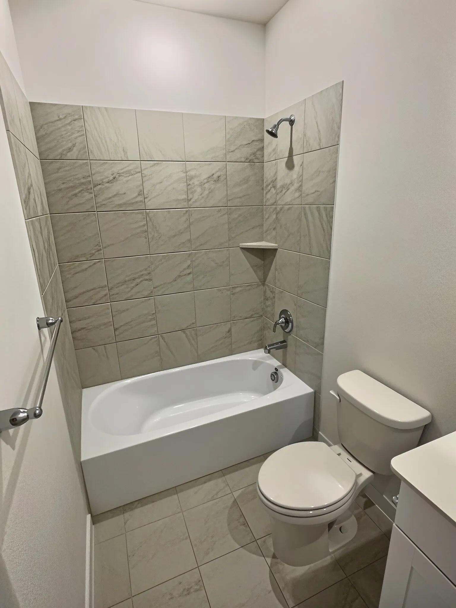 Bathroom featuring a white bathtub, tiled shower surround with built-in shelf, chrome fixtures, and coordinating floor tile