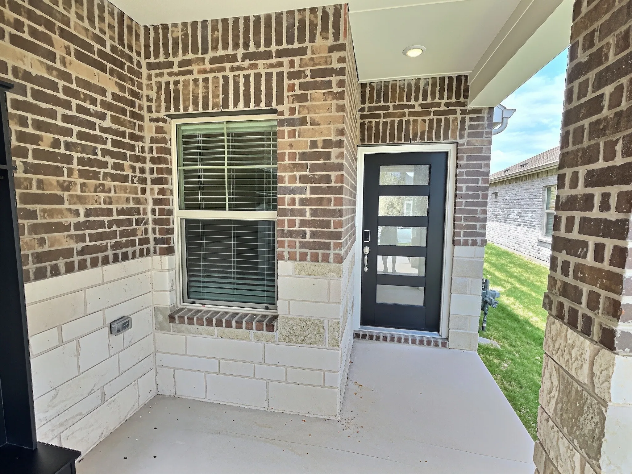 Brick and stone exterior with a modern black entry door featuring five glass panels, recessed lighting, and a front window with blinds